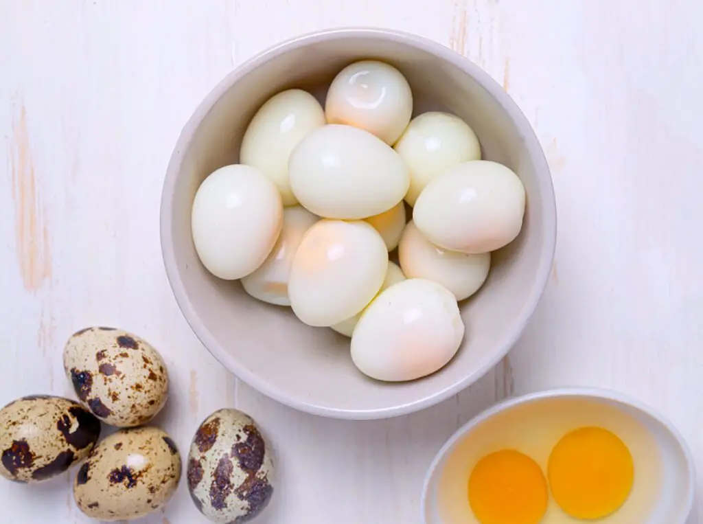 hard boiled coturnix quail eggs next to raw quail eggs in bowl