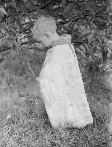 Great Depression black & white photo of a dirty toddler picking berries from a bush