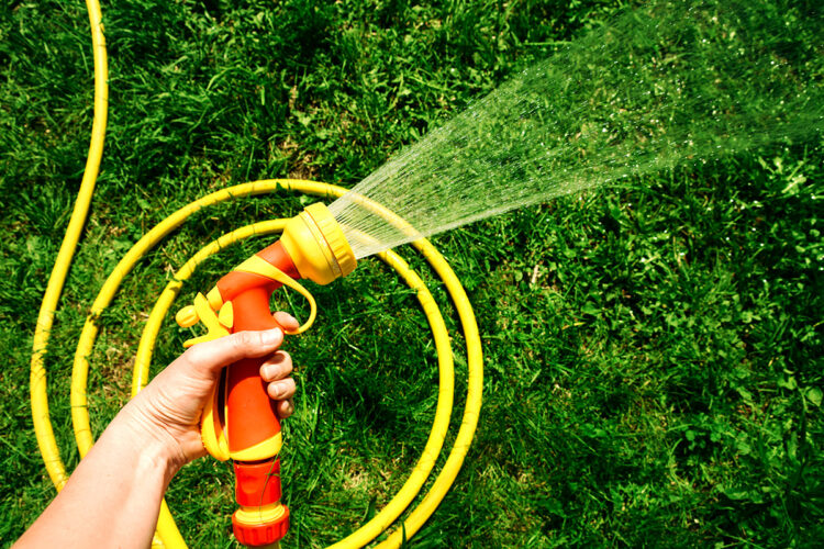 a yellow watering hose with an orange nozzle spraying water